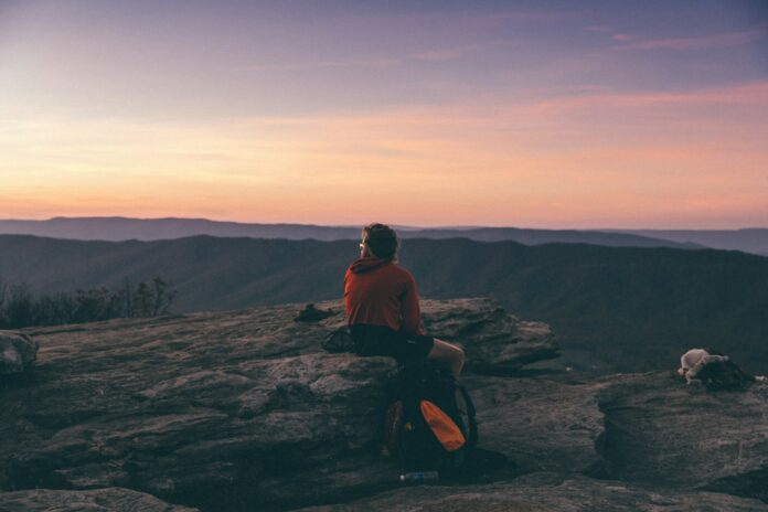 Photo by Emma Frances Logan person sitting on boulder overlooking mountain during golden hour