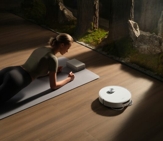 만성피로, 알아두면 건강 지키는 첫걸음 Woman planks on mat near robot vacuum cleaner.